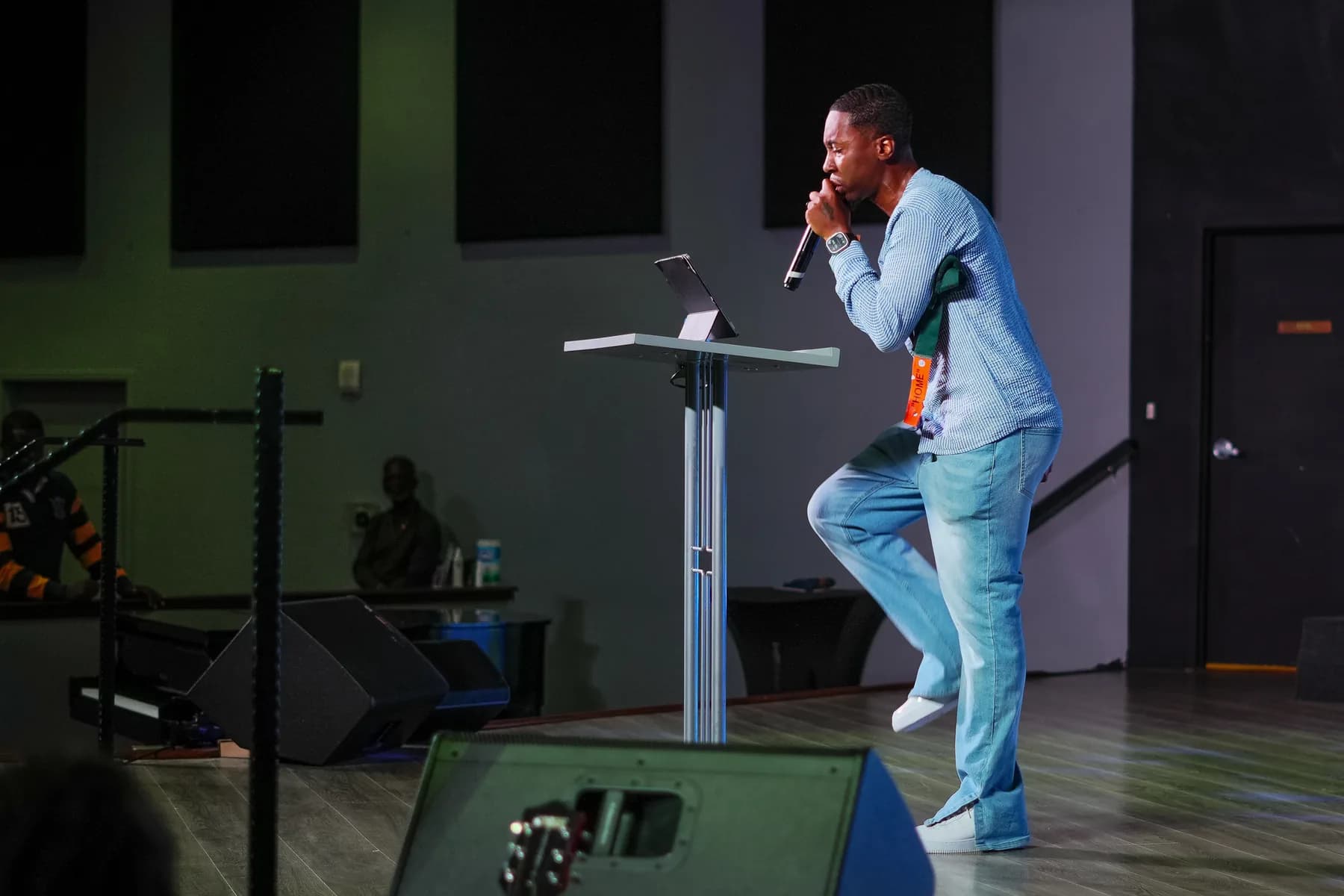 A preacher in light denim speaks from the stage with a microphone