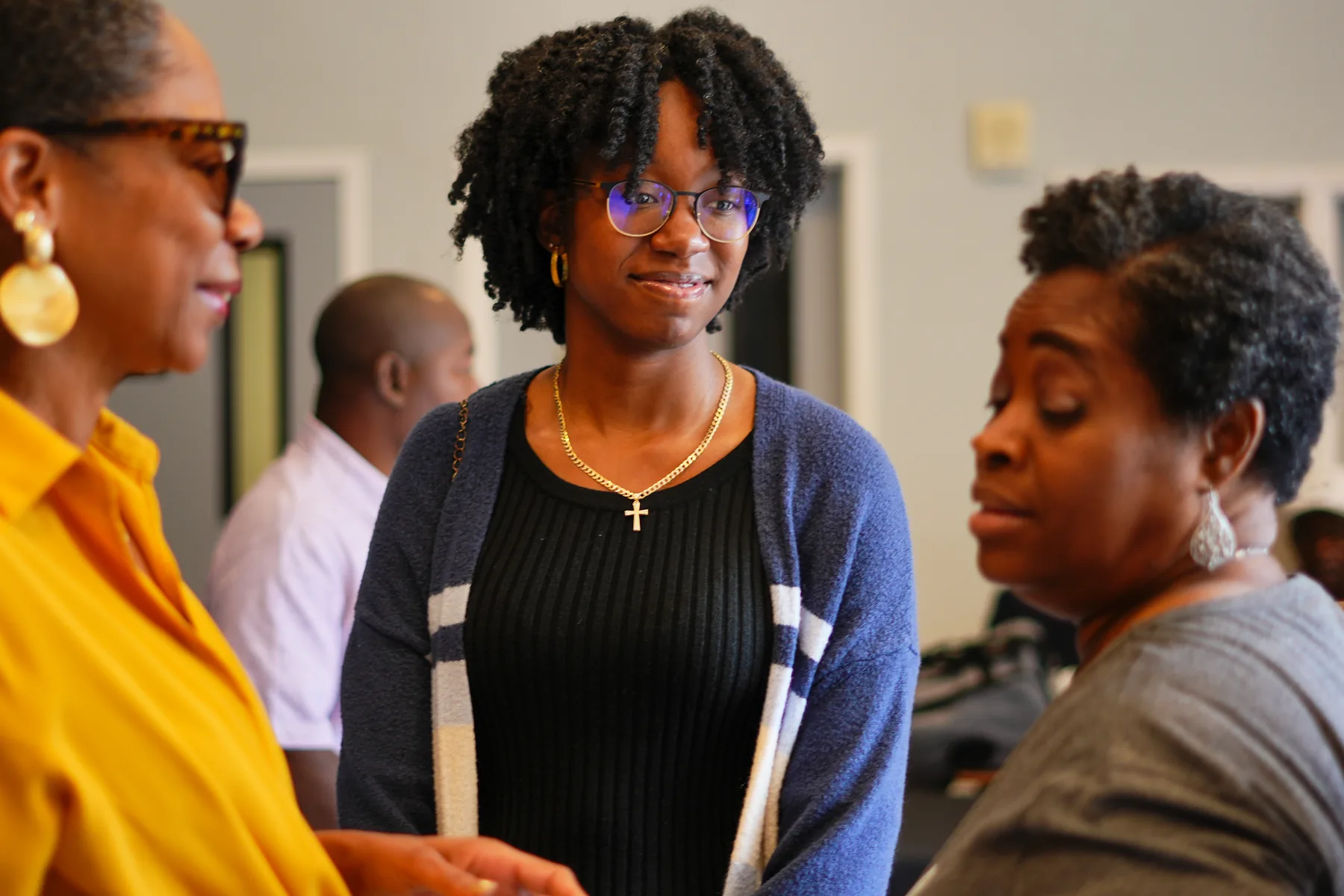 Three women talking together after a service, one wearing a gold earring and yellow top