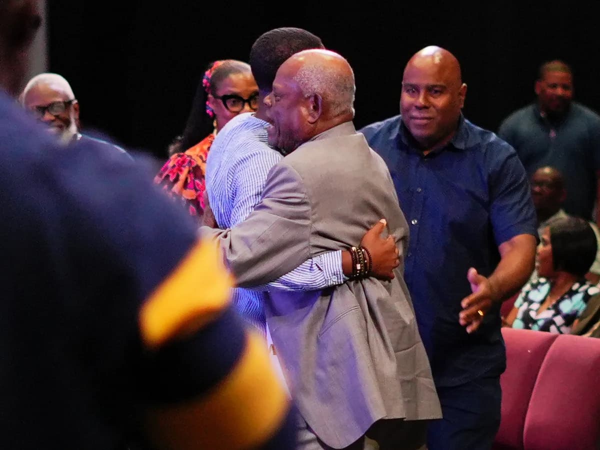 Two men embracing in the aisle after a service while others greet one another around them, with the congregation seated behind