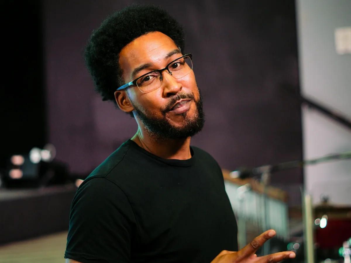 A man in a black T-shirt and glasses turning to smile at the camera inside the Solid Rock auditorium