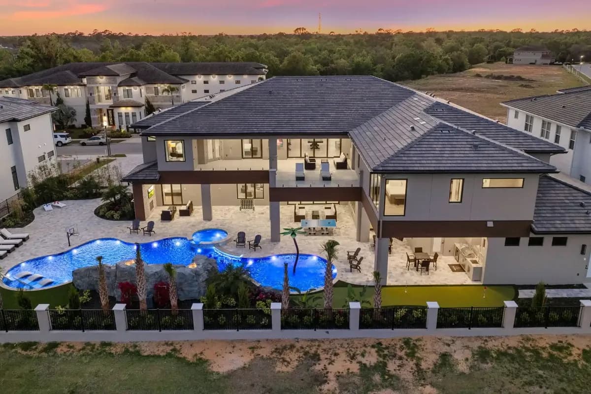 Aerial view at dusk of The Grove, a large vacation home at Reunion Resort near Orlando, with a lit pool, hot tub and putting green