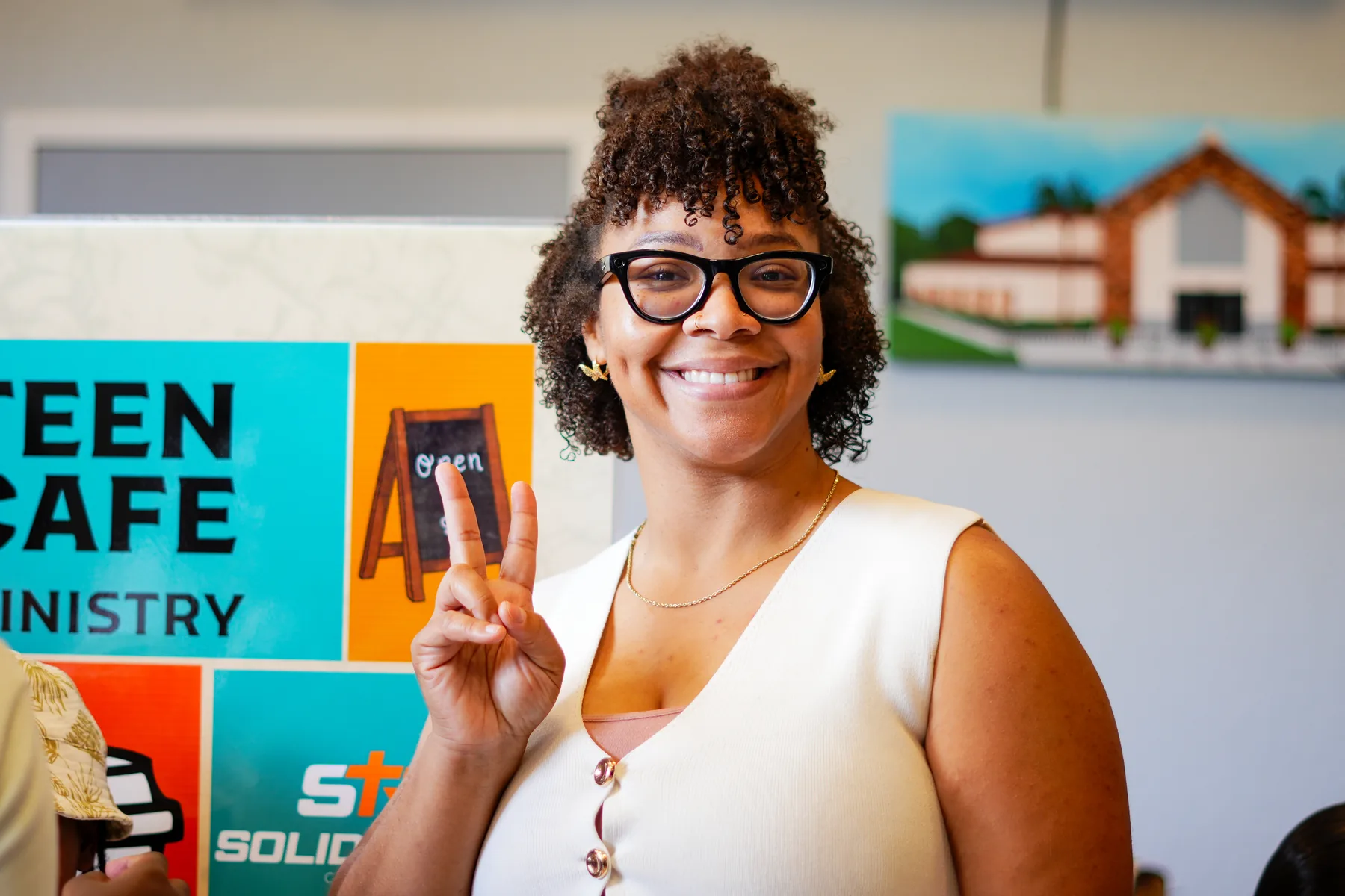 A smiling woman standing in front of the Teen Cafe Ministry sign