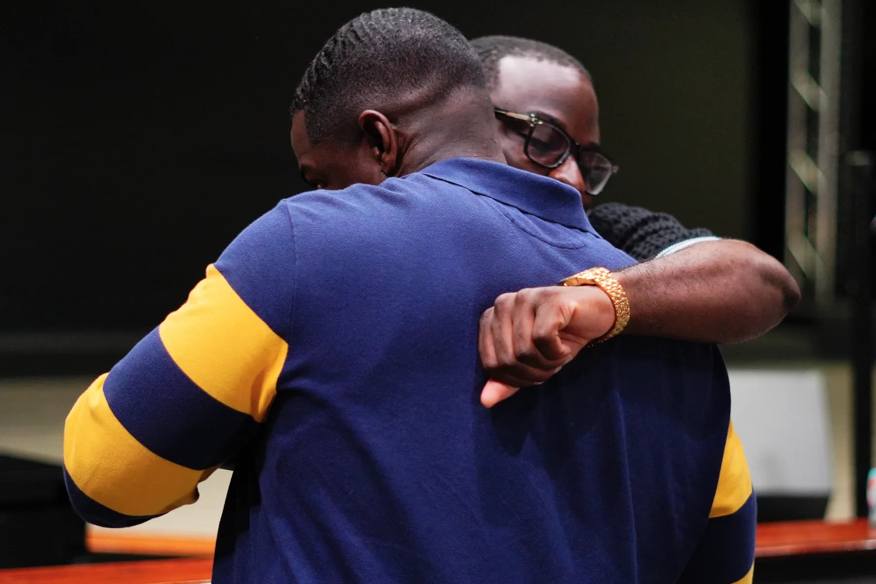 Two men greeting each other with an embrace inside the sanctuary, one wearing a navy and gold polo shirt