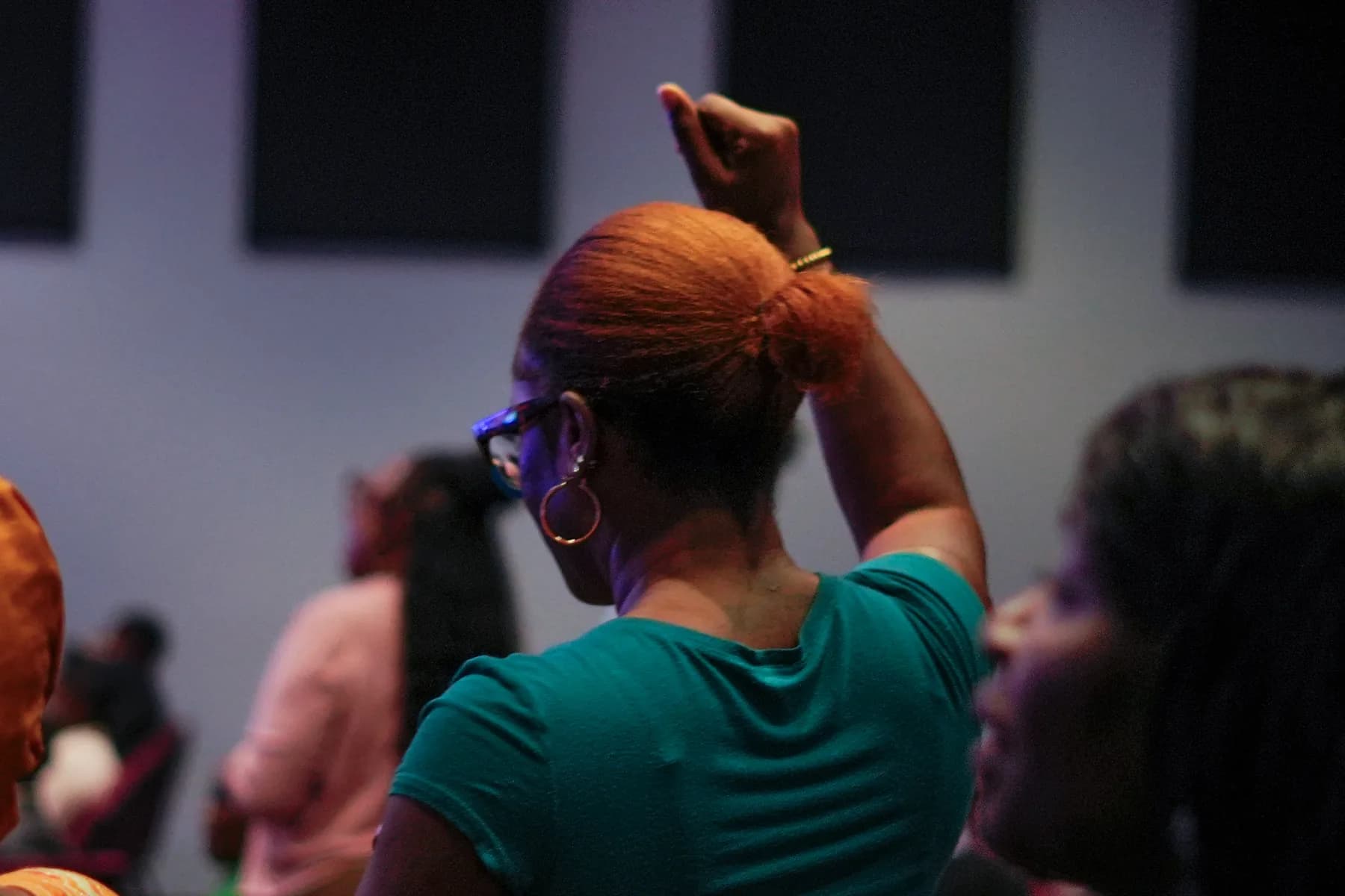 A woman in green raises her hand in worship among the congregation