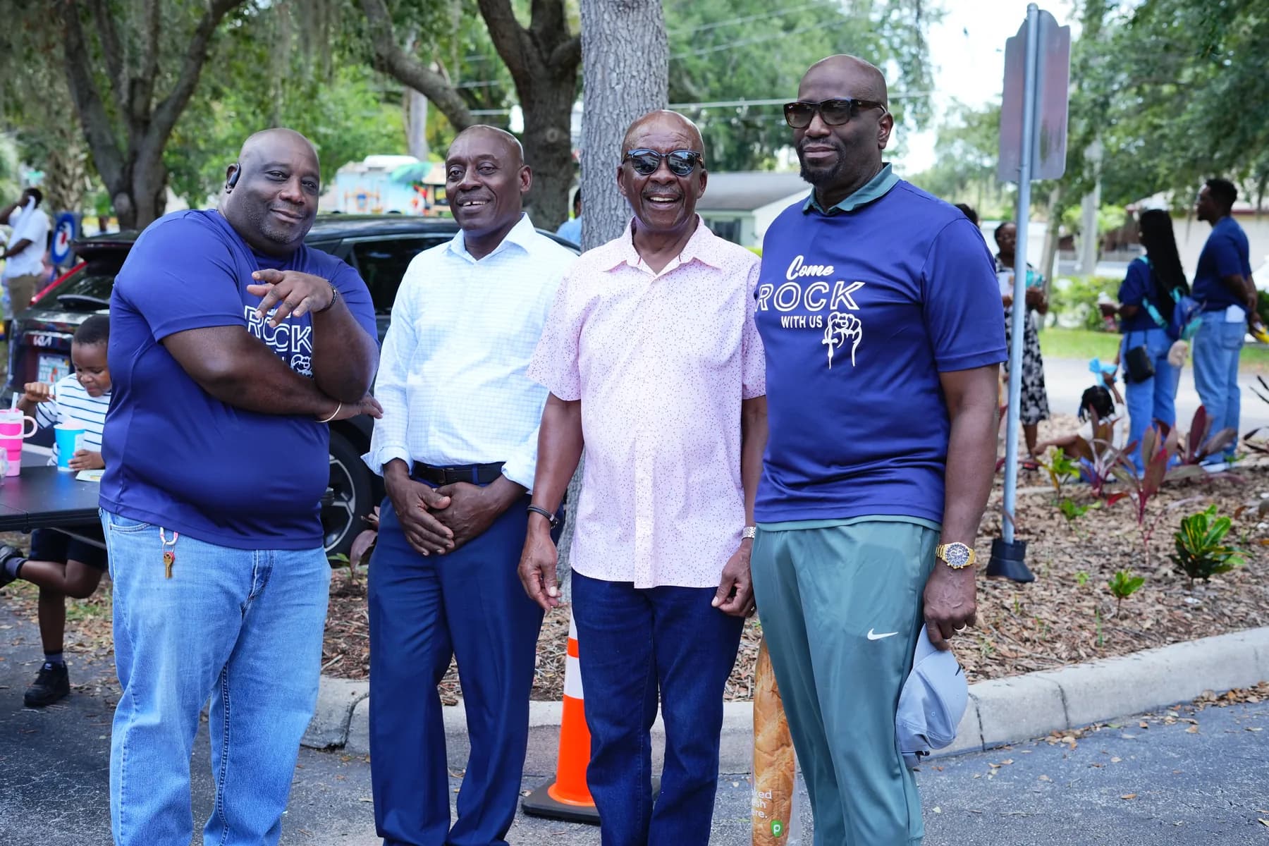 Four men in Solid Rock shirts standing together outdoors at a community event